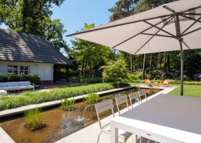 moderne bostuin met vijver en oranje stoelen sparq tuinen
